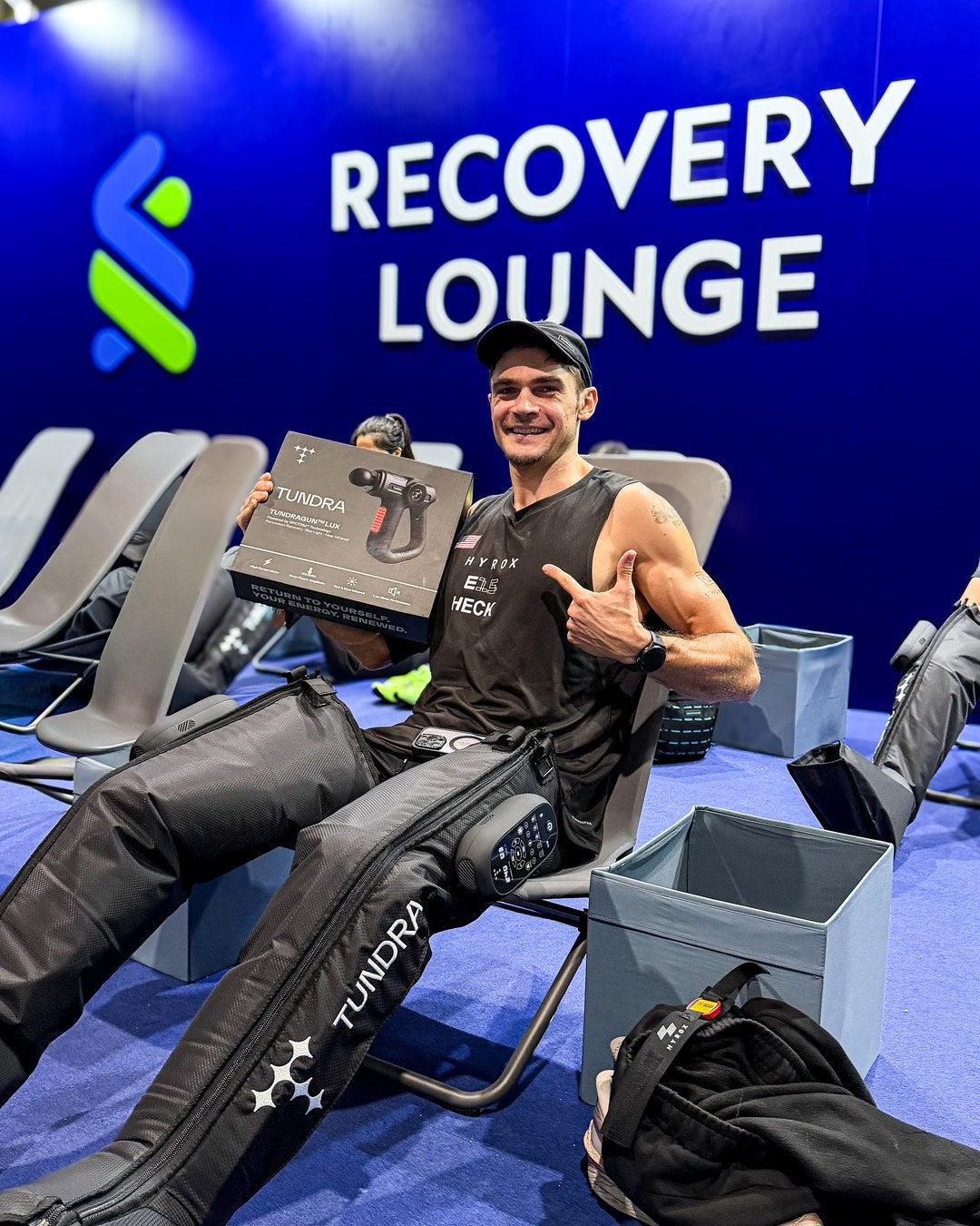 Athlete recovering with FLUX compression boots and TUNDRAgun in the Standard Chartered Recovery Lounge at HYROX Hong Kong 2026