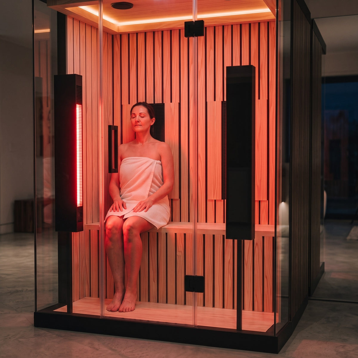 A session in the Valo, seated on one side of the hemlock bench facing a red light panel that is switched on